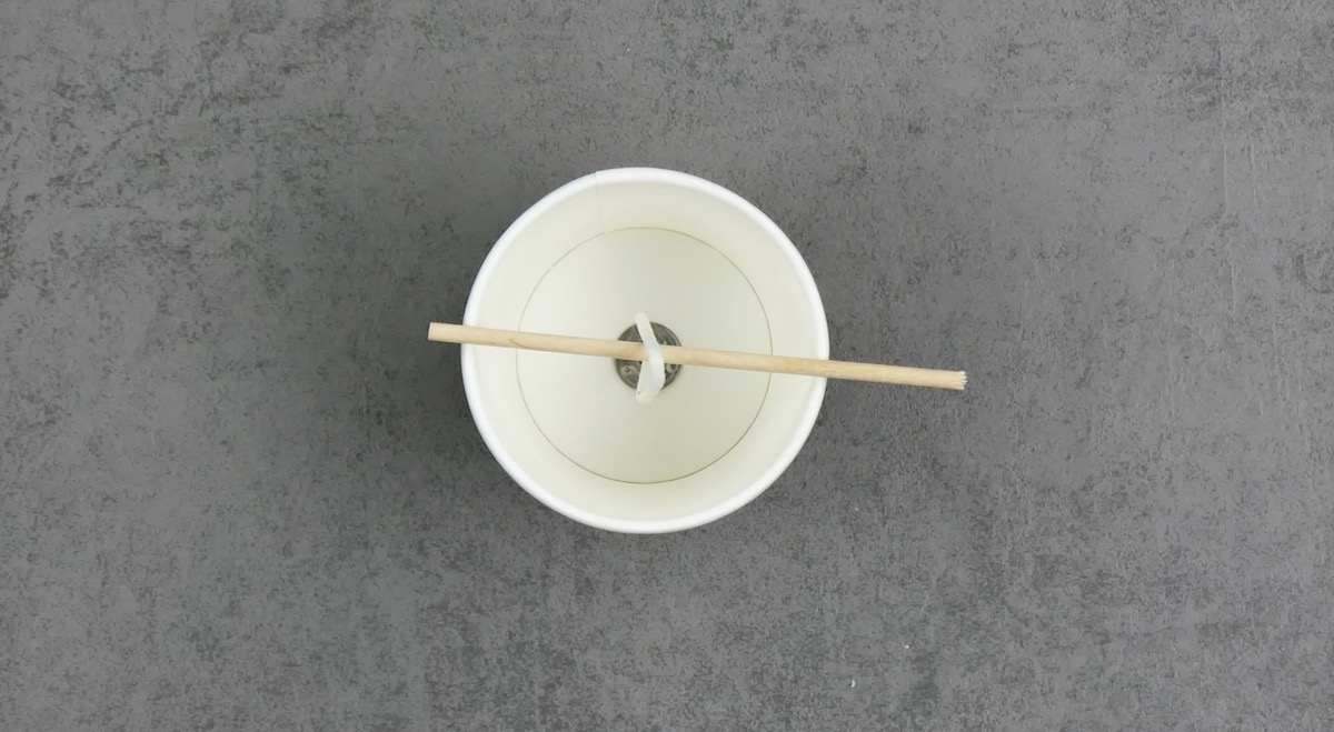 mèche au centre d'un gobelet en plastique attachée à un bâtonnet en bois pour la maintenir en place.